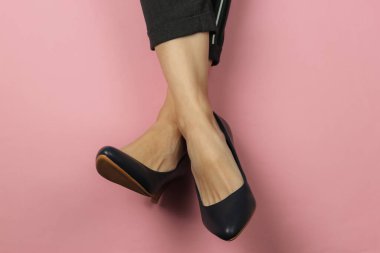 Pantolon giymiş kadın bacakları ve pembe pastel arka planda topuklu klasik ayakkabılar. Üst Manzara. Güzellik ve moda stüdyosu