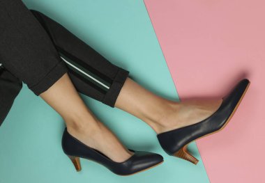 Pantolon giymiş kadın bacakları ve pembe mavi pastel arka planda topuklu klasik ayakkabılar. Üst Manzara. Güzellik ve moda stüdyosu