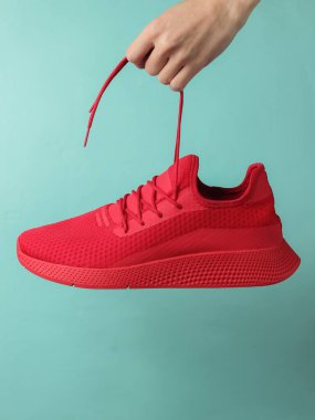 El, mavi pastel arka plandaki bağcıkların yanındaki kırmızı spor ayakkabısını tutuyor. Stüdyo çekimi