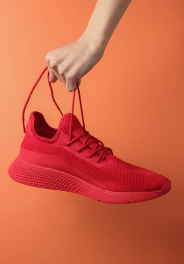 El, kırmızı spor ayakkabısını turuncu arka plandaki bağcıklardan tutuyor. Stüdyo çekimi