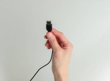 Kadın eli beyaz arka planda USB kablosu tutuyor. Stüdyo çekimi