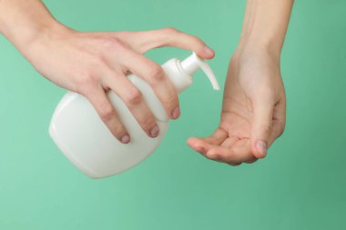 Minimalizm güzellik konsepti. Kadın eli mavi arka planda bir şişe krem tutuyor. Temiz ve yumuşak bir ten. Sağlık ve güzellik kavramı. Stüdyo çekimi