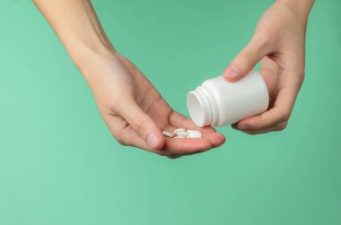 Kadın eli beyaz ilaç şişesi ve mavi arka planda haplar tutuyor. Sağlığa. Hastalık. 