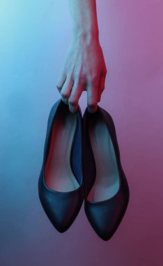 Kadınların elleri klasik yüksek topuklu ayakkabıları tutar. Yaratıcı pop sanatının pembe neon rengi. Moda eğilimli aydınlatma. Gece lambası