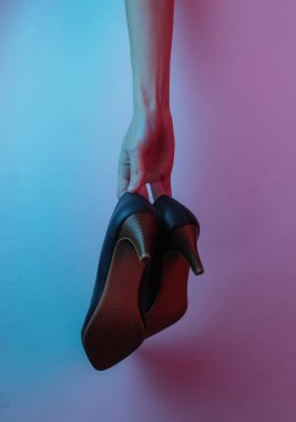 Kadınların elleri klasik yüksek topuklu ayakkabıları tutar. Yaratıcı pop sanatının pembe neon rengi. Moda eğilimli aydınlatma. Gece lambası