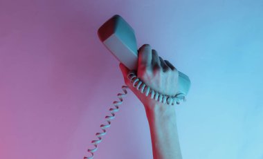 Kabloya sarılmış bir kadın el retro cep telefonunu tutuyor. Yaratıcı pop sanatının pembe neon rengi. Moda eğilimli aydınlatma. Gece lambası