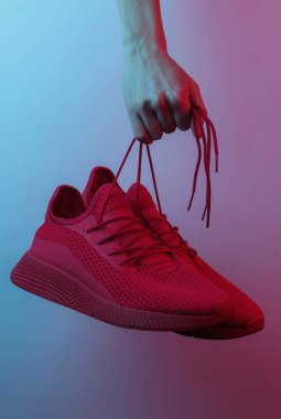 Kadın eli kırmızı spor ayakkabılarını bağcıklarından tutar. Yaratıcı pop sanatının pembe neon rengi. Moda eğilimli aydınlatma. Gece lambası