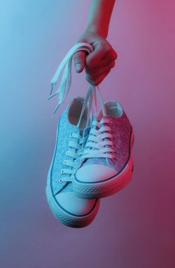 Kadın eli ayakkabıları bağcıklarından tutuyor. Yaratıcı pop sanatının pembe neon rengi. Moda eğilimli aydınlatma. Gece lambası