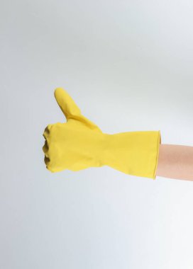 Ev temizliği konsepti. Kadın elleri, temizlik için sarı lastik eldiven giyer. Gri bir arka planda işaret parmağı gösterir.
