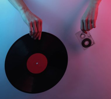 Retro dalga 80 'ler. Eller vinil plak ve ses kasetini tutuyor. Yaratıcı pop sanatının pembe neon rengi. Moda eğilimli aydınlatma. Gece lambası