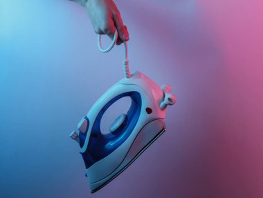 Kabloyla ütülemek için el demiri tutuyor. Yaratıcı pop sanatının pembe neon rengi. Moda eğilimli aydınlatma. Gece lambası