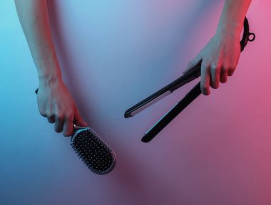 El, saç düzleştirici ve tarak tutuyor. Yaratıcı pop sanatının pembe neon rengi. Moda eğilimli aydınlatma. Gece lambası