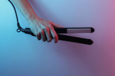 El, saç düzleştiricisini tutuyor. Yaratıcı pop sanatının pembe neon rengi. Moda eğilimli aydınlatma. Gece lambası