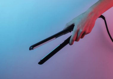 El, saç düzleştiricisini tutuyor. Yaratıcı pop sanatının pembe neon rengi. Moda eğilimli aydınlatma. Gece lambası