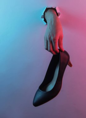 Yırtık bir delikten yüksek topuklu ayakkabı tutarak. Yaratıcı pop sanatının pembe neon rengi. Moda eğilimli aydınlatma. Gece lambası