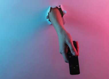 Uzaktan kumandayı yırtık delikten tutarak. Yaratıcı pop sanatının pembe neon rengi. Moda eğilimli aydınlatma. Gece lambası