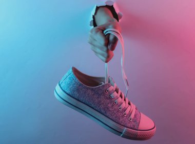 Yırtık delikten el ele tutuşan spor ayakkabısı. Yaratıcı pop sanatının pembe neon rengi. Moda eğilimli aydınlatma. Gece lambası
