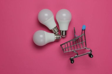 Pembe arka planda üç LED ampul ve alışveriş arabası. Üst görünüm