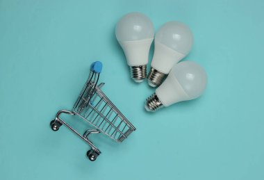 Mavi arka planda üç LED ampul ve alışveriş arabası. Üst görünüm