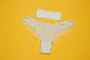 Kadın külotu ve sarı arka planda ped. Kadın hijyeni konsepti. Kritik günler, adet günleri. Üst Manzara. Düz yatıyordu