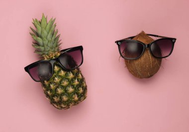 Yaz dönemi. Eğlence ve mizah anlayışı. Ananas ve Hindistan cevizi, pembe pastel arka planda güneş gözlüğü.