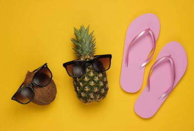 Yaz dönemi. Eğlence ve mizah anlayışı. Plaj tatil. Güneş gözlüklü ananas ve hindistan cevizi, flopson sarısı arka plan