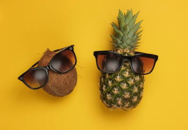 Yaz dönemi. Eğlence ve mizah anlayışı. Sarı arka planda güneş gözlüklü ananas ve hindistan cevizi.