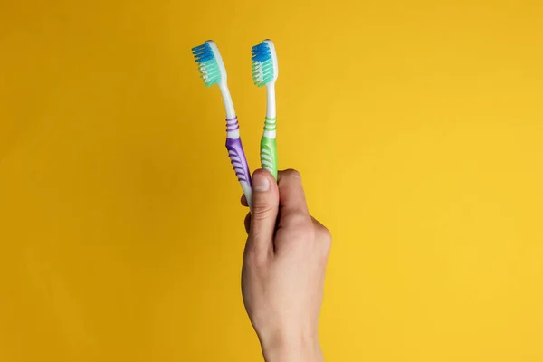 Mano Femenina Sostiene Dos Cepillos Dientes Sobre Fondo Amarillo Concepto — Foto de Stock