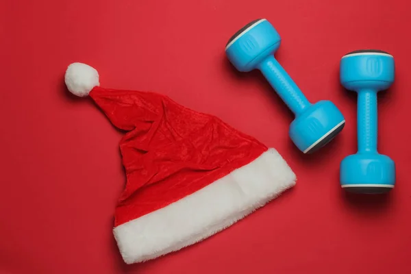Kapelusz Mikołaja Hantlami Czerwonym Tle Koncepcja Fitness Święta Bożego Narodzenia — Zdjęcie stockowe
