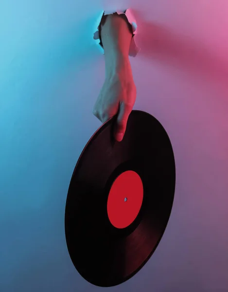 Hand holding vinyl plate through torn hole. Creative pop art pink blue neon color. Trendy gradient illumination. Night light