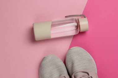 Düz konsept, sağlıklı yaşam tarzı, spor ve zindelik. Koşmak için spor ayakkabıları, pembe pastel arka planda bir şişe su. Üst görünüm