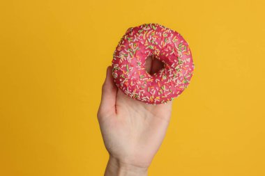 Kadın eli sarı arka planda jöleli donut tutuyor. Tatlı tatlı. Üst görünüm.