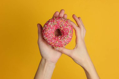 Sarı arka planda jöleli çörek tutan kadın eller. Tatlı tatlı. Üst görünüm.