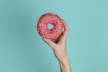 Kadın eli mavi arka planda jöleli donut tutuyor. Pastel renk eğilimi. Üst görünüm.