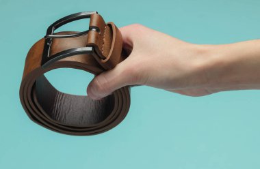 Kadının elinde mavi arka planda kahverengi deri bir kemer var.