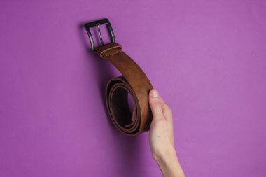 Kadının elinde mor arka planda deri kahverengi bir kemer var.