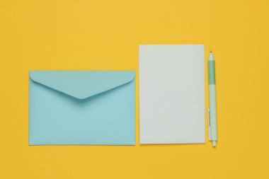 Zarfta sarı arka planda bir mektup ve kalem var. Sevgililer günü, düğün ya da doğum günü. Üst görünüm