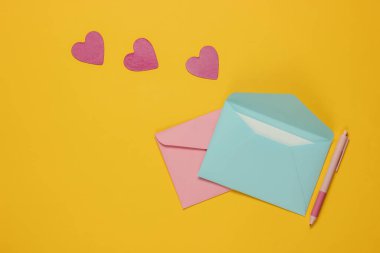 Zarfta bir mektup, kalem, sarı arka planda dekoratif kalpler. Sevgililer günü, düğün ya da doğum günü için düz yatış.