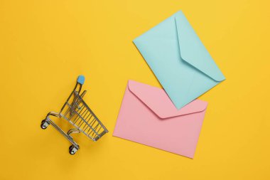 Pembe ve mavi. Sarı arka planda iki zarf ve alışveriş arabası. Sevgililer günü, düğün ya da doğum günü için maket