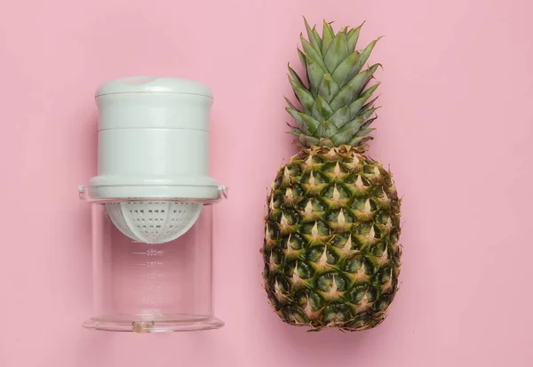 Plastic manual juicer and pineapple on pink pastel background. The concept of healthy nutrition, weight loss. Freshly squeezed juices. Top view