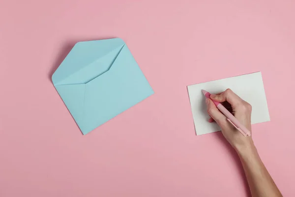 女性の手はピンクのパステルの背景にペンで手紙を書きます 結婚式の招待状ラブレターバレンタイン トップ表示 — ストック写真