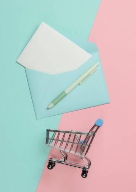 Zarfta mektup ve pembe mavi pastel arka planda alışveriş arabası var. Sevgililer günü, düğün ya da doğum günü için bir model. Üst görünüm