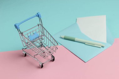 Zarfta mektup ve pembe mavi pastel arka planda alışveriş arabası var. Sevgililer günü, düğün ya da doğum günü için maket.