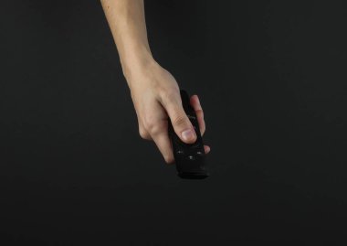 Kadın eli siyah arkaplanda televizyon uzaktan kumandası tutuyor