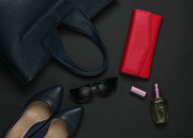 Siyah arka planda kadın aksesuarları. Yüksek topuklu ayakkabılar, deri çanta, çanta, güneş gözlüğü, parfüm şişesi. Üst görünüm