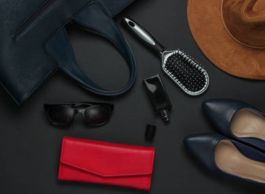 Siyah arka planda kadın aksesuarları. Şapka, deri çanta, tarak, güneş gözlüğü, parfüm şişesi. Üst görünüm