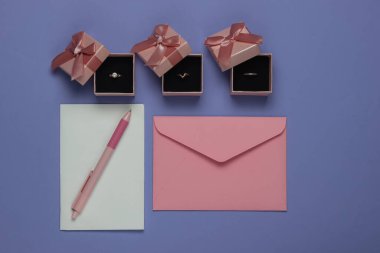 Hediye kutularında altın yüzükler, mor arka planda düğün davetiyeleri olan bir zarf. Üst Manzara. Düz yatıyordu