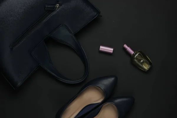 Women's accessories on a black background. High heel shoes, leather bag, perfume bottle. Top view
