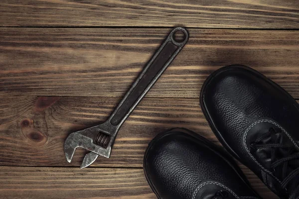 Work leather shoes and wrench. Industrial working tools and instruments, safety equipmen on wooden background. Top view