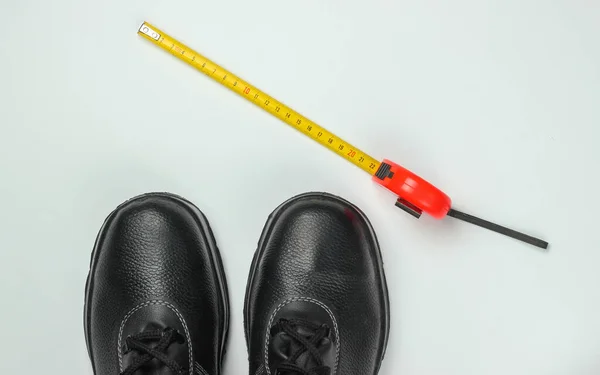 Work leather shoes and measuring meter ruler on white background. Safety gear and industrial tool. Top view